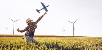 Boy playing with a model airplane in a cornfield with wind turbines in the background
