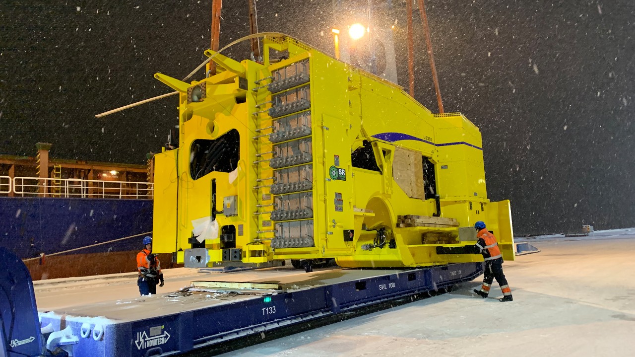 Trabajadores cargando la pieza de una enorme máquina industrial bajo la nieve